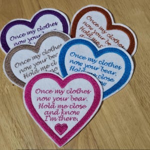 May include: Five heart-shaped embroidered patches with the text "Once my clothes now your bear. Hold me close and know I'm there." in different colours, including pink, blue, brown, orange, and purple.