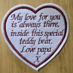 May include: A white heart-shaped patch with a claret border and embroidered text. The text reads "My love for you is always there, inside this special teddy bear. Love papa X."
