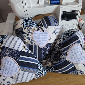 May include: Three blue and white patchwork heart-shaped cushions with embroidered messages. The messages read "Made from clothes I used to wear Hold me close I'll be there. Nan".