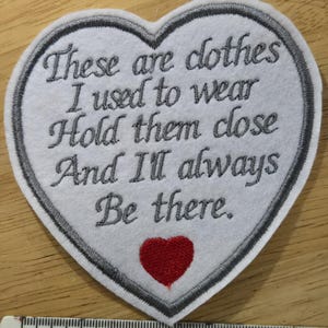 Puede incluir: Un parche en forma de coraz&oacute;n con texto bordado: "These are clothes I used to wear Hold them close And I'll always Be there." El parche tiene un fondo blanco, un borde gris y un coraz&oacute;n rojo. Una regla muestra las medidas en cent&iacute;metros.