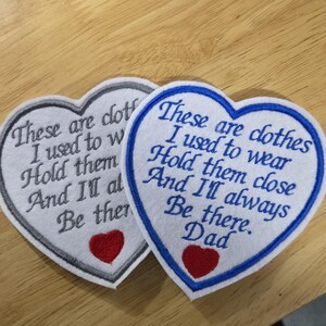 Puede incluir: Dos parches bordados en forma de coraz&oacute;n. Uno tiene un borde gris, el otro un borde azul. Ambos tienen el texto "These are clothes I used to wear Hold them close And I'll always Be there." y un coraz&oacute;n rojo.