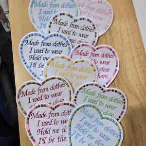 May include: A collection of heart-shaped fabric patches featuring embroidered text that reads, Made from clothes I used to wear, Hold me close, I'll be there, XX. Each patch has a colourful, multi-striped border and white background with varied thread colours.