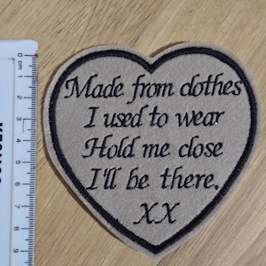 May include: A beige heart-shaped patch with black embroidered text that reads "Made from clothes I used to wear Hold me close I'll be there. XX".
