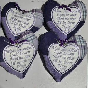 May include: Four heart-shaped fabric cushions in shades of purple and plaid. Each cushion features a white heart-shaped patch with purple embroidered text: Made from clothes I used to wear, Hold me close, I'll be there, Nain, XX.