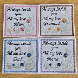 May include: Four white felt squares with embroidered messages. Each square has a different coloured border and floral design. The messages read: "Always beside you All my love Mum", "Always beside you All my love Grandad", "Always beside you All my love Dad", and "Always beside you All my love Nana".
