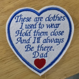 Puede incluir: Un parche en forma de coraz&oacute;n con un centro blanco y un borde azul. El parche presenta texto bordado en azul, que dice: "These are clothes I used to wear Hold them close And I'll always Be there. Dad." Un coraz&oacute;n rojo en la parte inferior.