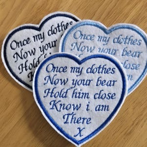 May include: Three white felt heart-shaped patches with blue embroidered edges. The patches have the text "Once my clothes now your bear hold him close know I am there X" embroidered in blue thread.