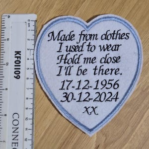 May include: A white heart-shaped patch with blue edging, embroidered with the text "Made from clothes I used to wear Hold me close I'll be there. 17-12-1956 30-12-2024 XX".