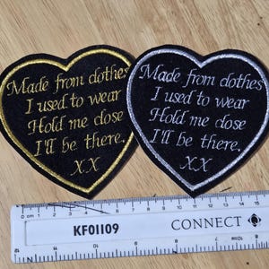 Pode incluir: Dois patches em forma de cora&ccedil;&atilde;o com texto bordado. Um tem acabamento e letras douradas, o outro prateado. O texto diz: "Made from clothes I used to wear, Hold me close, I'll be there, XX."