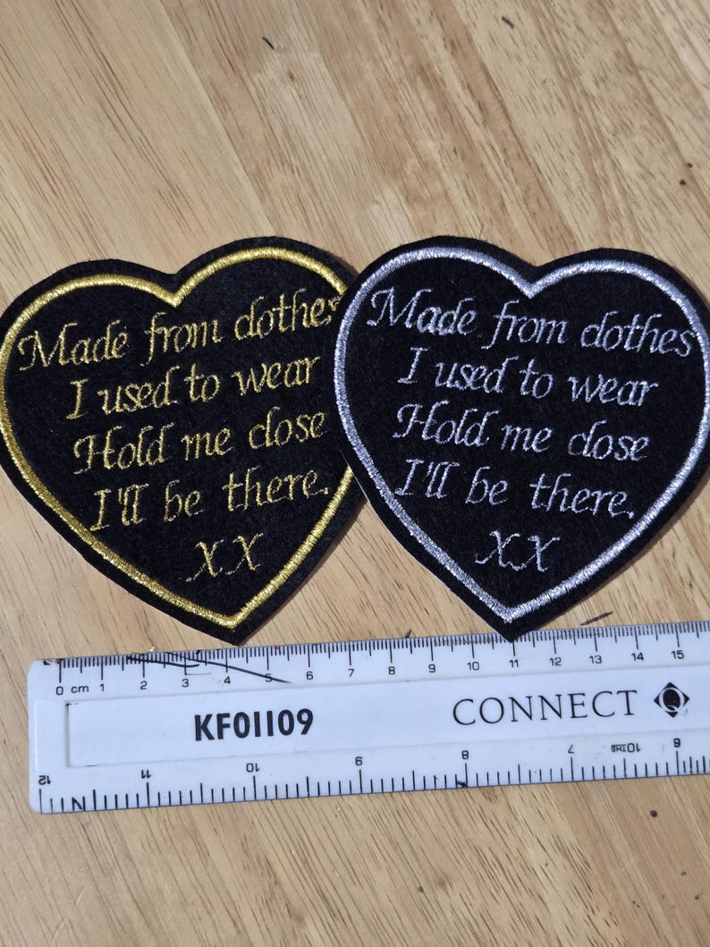 Pode incluir: Dois patches em forma de cora&ccedil;&atilde;o com texto bordado. Um tem acabamento e letras douradas, o outro prateado. O texto diz: "Made from clothes I used to wear, Hold me close, I'll be there, XX."