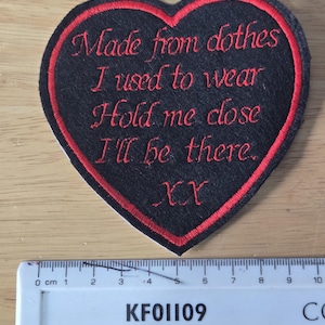 May include: A heart-shaped patch with a black background and a red border. The patch features red embroidered text that reads "Made from clothes I used to wear Hold me close I'll be there. XX". A ruler is below the patch.