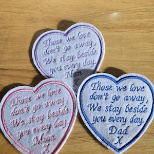 May include: Three felt heart-shaped patches with embroidered messages. The top patch is purple and says "Those we love don't go away, We stay beside you every day. Nan X". The middle patch is pink and says "Those we love don't go away, We stay beside you every day. Mum X". The bottom patch is blue and says "Those we love don't go away, We stay beside you every day. Dad X".