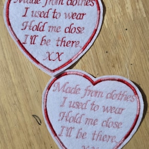 May include: Two heart-shaped patches with red trim and embroidered text. The text reads "Made from clothes I used to wear Hold me close I'll be there XX". The patches are white with red embroidery.