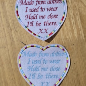 May include: Two heart-shaped patches with embroidered text. The patches are white with a colourful border and the text "Made from clothes I used to wear Hold me close I'll be there. XX".