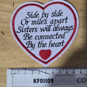 May include: Heart-shaped patch with the text "Side by side Or miles apart Sisters will always Be connected By the heart." The patch has a white background with a red border and a small red heart. The patch is approximately 7.6 cm wide.