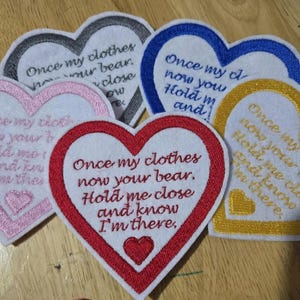 May include: Five heart-shaped embroidered patches with different coloured borders. The patches have the same text: "Once my clothes now your bear. Hold me close and know I'm there."