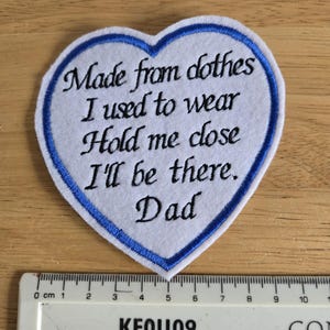 May include: White heart-shaped patch with blue stitching. The patch has the text "Made from clothes I used to wear Hold me close I'll be there. Dad" embroidered in black thread.