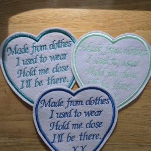 May include: Three heart-shaped embroidered patches. The patches are white with blue, green, and blue borders. The text reads "Made from clothes I used to wear, Hold me close, I'll be there."