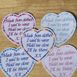 May include: Five heart-shaped patches with embroidered text. Each patch features the phrase "Made from clothes I used to wear Hold me close I'll be there XX." The patches have different colored borders.
