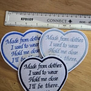 May include: Three white heart-shaped fabric patches with blue embroidery. The patches have the text "Made from clothes I used to wear Hold me close I'll be there." The bottom patch also has the text "XX".