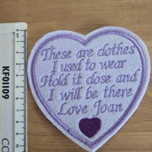 May include: A white heart-shaped patch with purple embroidery. The patch says "These are clothes I used to wear Hold it close and I will be there Love Joan".