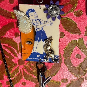 May include: A vintage postcard with a cartoon boy in a blue shirt and shorts, a kangaroo, and the text "Route de la Princesse". The postcard is attached to a chain with a purple flower charm and a white leaf charm.