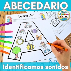 May include: A worksheet with the Spanish word "ABECEDARIO" at the top, featuring the letter "A" with illustrations to color. Includes a rainbow, ambulance, and bee. The text "Identificamos sonidos" is at the bottom. Colored markers and a hand holding a crayon are visible.