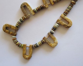 May include: A brown and green stone necklace with a unique design. The necklace features a series of U-shaped stones interspersed with smaller round stones.