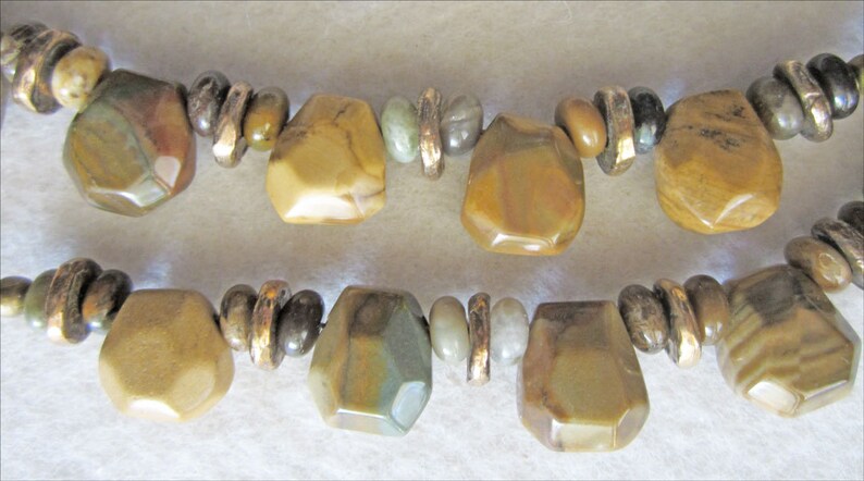 May include: A multi-strand necklace with brown, green, and gold beads. The beads are irregularly shaped and have a natural, earthy look.