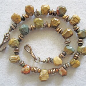 May include: A necklace made with brown, green, and white patterned stone beads and copper spacer beads. The necklace has a hook clasp.