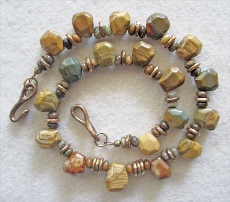 May include: A necklace made with brown, green, and white patterned stone beads and copper spacer beads. The necklace has a hook clasp.