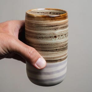 Può includere: Una tazza in ceramica marrone e bianca con un motivo a righe. La tazza ha una base larga e una parte superiore leggermente rastremata.