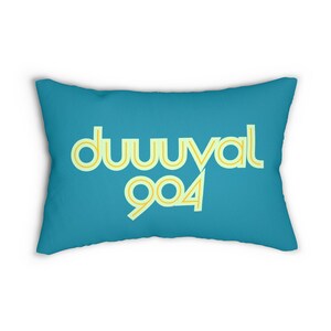 May include: A teal blue throw pillow with the text "duuuval 904" in yellow and light green lettering.