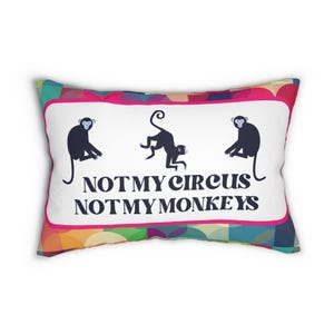 Könnte beinhalten: Ein weißes Kissen mit einem bunten geometrischen Muster auf der Rückseite. Die Vorderseite des Kissens hat einen weißen Hintergrund mit drei schwarzen Affen und dem Text "NOT MY CIRCUS NOT MY MONKEYS".