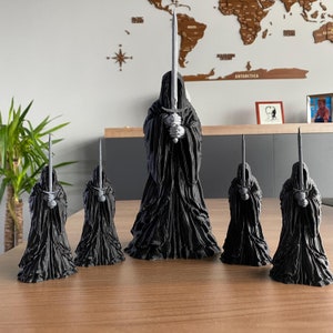 Op de afbeelding: Vijf zwarte, 3D-geprinte figuren van gekapte figuren die zwaarden vasthouden. De figuren zijn van verschillende grootte en zijn in een rij op een houten oppervlak gerangschikt.