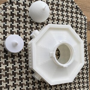 May include: White 3D printed model of a building with a domed roof. The model is in three pieces, the base, the dome, and a small circular piece.