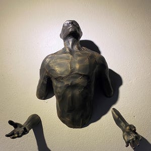 May include: A bronze sculpture of a human torso with outstretched arms, mounted on a wall. The sculpture is stylized and has a textured surface.