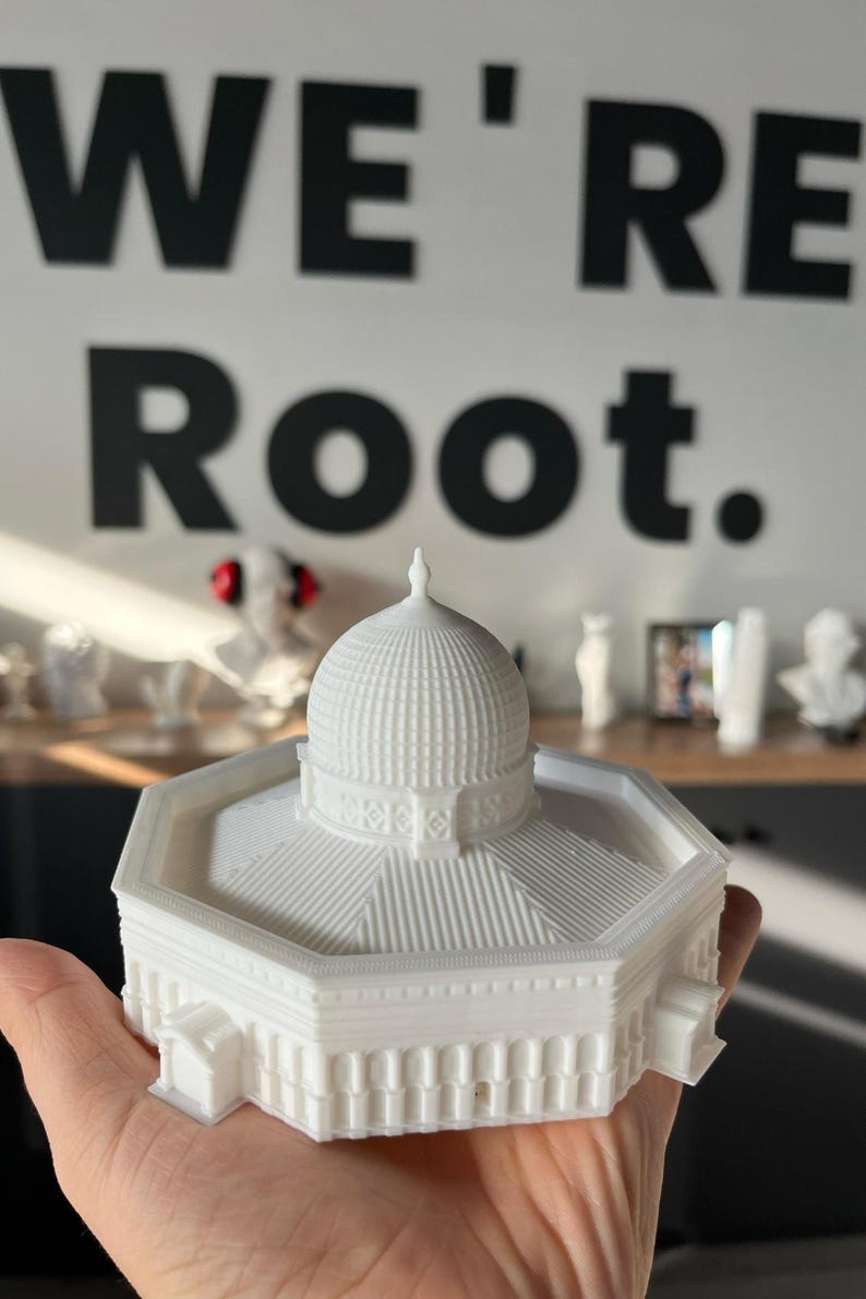 May include: White 3D printed model of a building with a domed roof. The model is sitting on a hand.