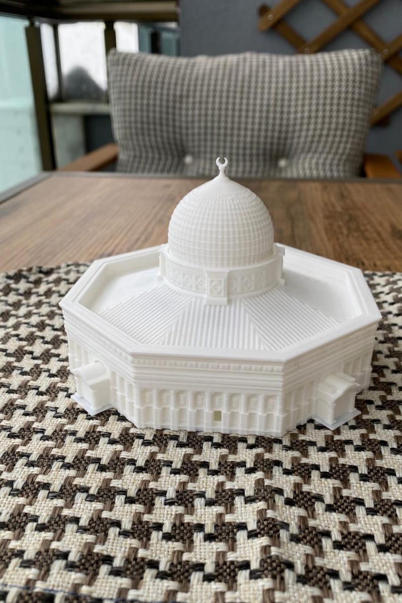 May include: White 3D printed model of a mosque with a domed roof and intricate details. The model is sitting on a patterned surface.