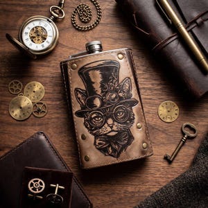 Op de afbeelding: Een steampunk-thema collectie met een met leer omwikkelde fles met een kattenontwerp, een zakhorloge, een notitieboek, een pen, een portemonnee, manchetknopen en een sleutel. De items zijn gerangschikt op een houten oppervlak, wat een vintage esthetiek creëert.