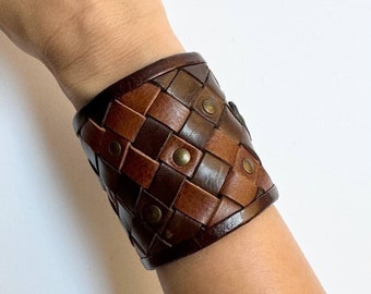 May include: A brown leather cuff bracelet with a woven design and metal studs.
