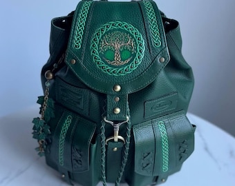 Può includere: Uno zaino testurizzato verde scuro con una patta superiore caratterizzata da un ricamo dell'albero della vita all'interno di un bordo a nodo celtico circolare. La borsa presenta due tasche frontali con finiture intrecciate e una chiusura centrale.