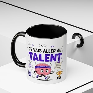 May include: A white ceramic mug with a black interior and handle. The exterior features a graphic of a pink brain wearing a purple headband with the text 'JE VAIS ALLER AU TALENT', 'PAS DE PLAN B', 'JUSTE PLAN A', and a checklist with 'RÊVER', 'TRAVAILLER', 'RÉUSSIR'.