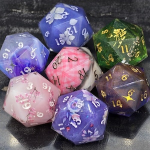Pode incluir: Um conjunto de sete dados de vinte lados em várias cores, incluindo azul, verde, rosa e roxo. Cada dado apresenta desenhos florais e numeração metálica. Para jogos de tabuleiro.