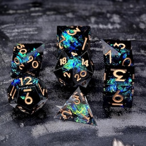 Könnte beinhalten: Ein Satz von sieben polyedrischen Würfeln in verschiedenen Formen, darunter ein d4, d6, d8, d10, d12, d20 und ein Prozentwürfel. Die Würfel sind schwarz mit irisierenden blau-grünen Einschlüssen und goldfarbenen Zahlen.