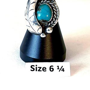 May include: A sterling silver ring featuring a central oval turquoise stone, a twisted rope border, and a leaf-shaped side detail with engraved veins. The ring is displayed with a label indicating a size 6 1/4.