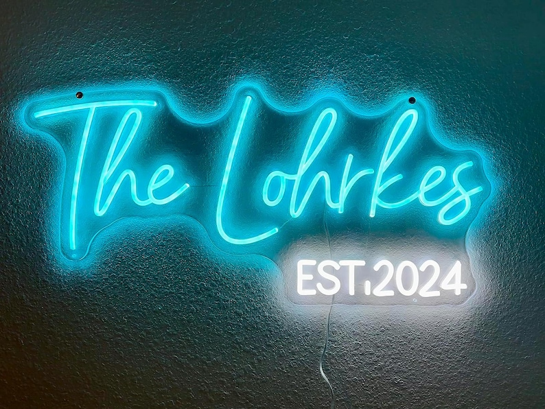 May include: A neon sign in a teal color displays the words "The Lohrkes" in a cursive font. Below, in a white rectangular box, the text "EST. 2024" is displayed. The sign is mounted on a textured teal wall.