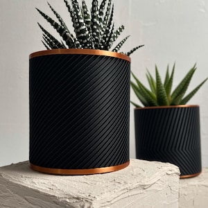 May include: Two black and copper plant pots with a geometric pattern. The pots are filled with green succulents.