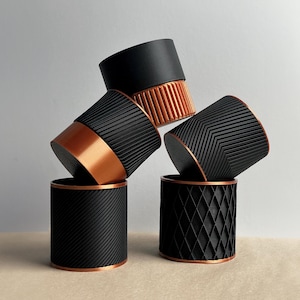 May include: Five black and copper planters with different geometric patterns. The planters are stacked on top of each other.