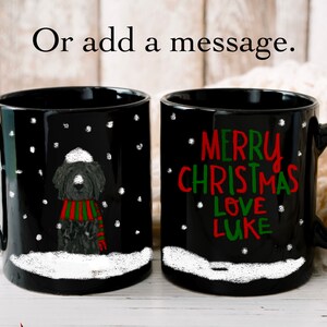 May include: Two black coffee mugs with white snow and snowflakes. One mug has a black and white illustration of a dog wearing a red and green scarf and a white hat. The other mug has the text "Merry Christmas Love Luke" in red and green.